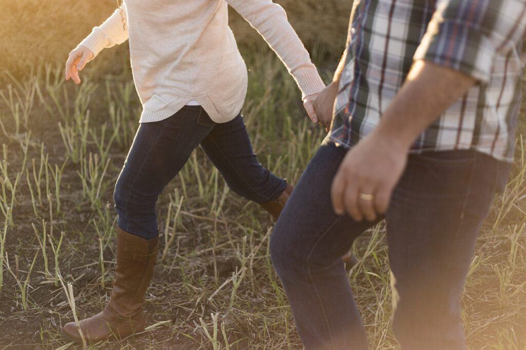 bodies of man and woman walking in field holding hands