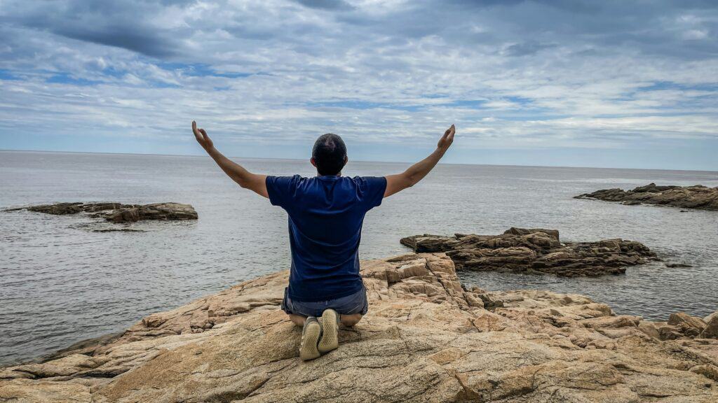 man on beach on knees arms lifted