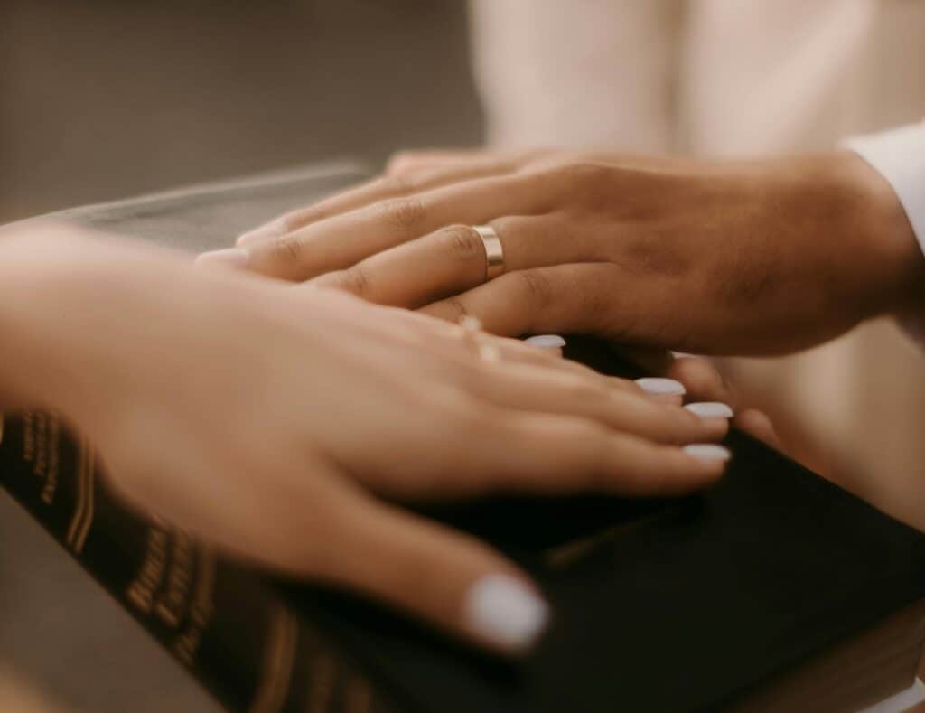 couple wearing rings with hands on the Bible
