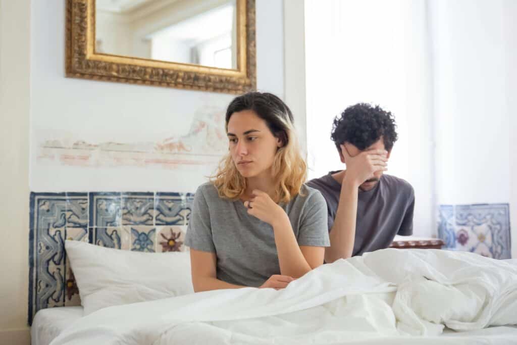 couple sitting up in bed husband covering eyes wife looking away