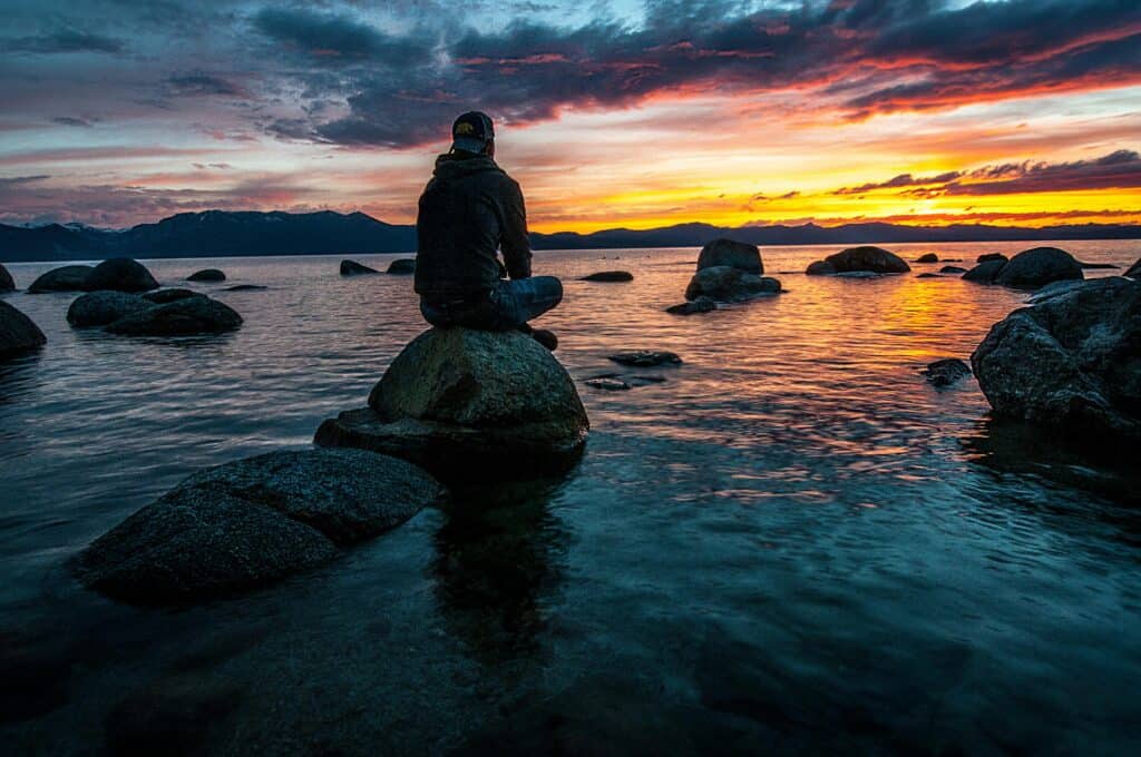 man sitting on rocks near beach at sunset