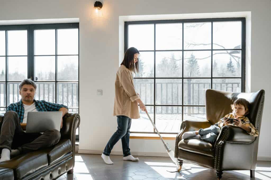 woman mopping while son and husband watch TV and phone